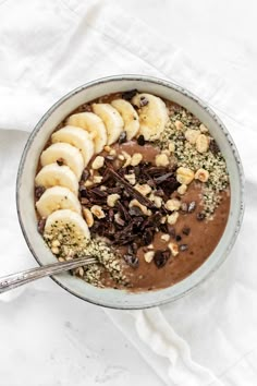 a bowl filled with chocolate and bananas on top of a white tablecloth next to a spoon