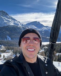 a man wearing sunglasses and a hat is holding a ski pole in front of snowy mountains