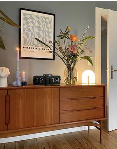 a vase with flowers on top of a wooden dresser next to a clock and candles