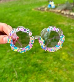 a person holding up some glasses with the words happy birthday on them in front of green grass