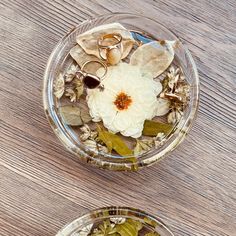 two clear bowls filled with flowers and leaves on top of a wooden table next to each other