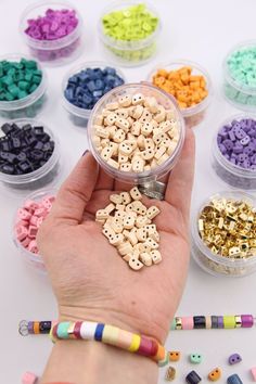 a hand holding a container filled with lots of different colored beads next to crayons