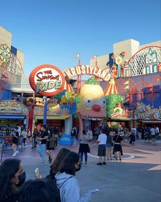 an amusement park with many people walking around and in the background there is a large balloon that looks like a clown