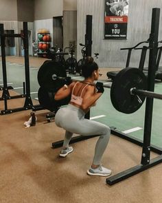 a woman squats in front of a barbell with one hand on her hip