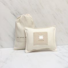 two pillows sitting next to each other on top of a white marble countertop with a drawstring bag