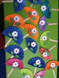 colorful paper flowers and leaves on sticks in front of a green board with stick holders