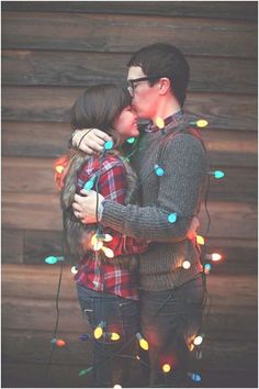 a man and woman standing next to each other with christmas lights on the wall behind them