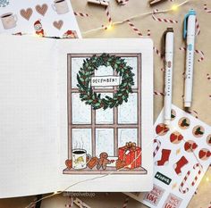 an open notebook with a christmas scene on the window sill and holiday decorations around it