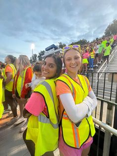 two women in safety vests standing next to each other at a sporting event with people watching from the bleachers