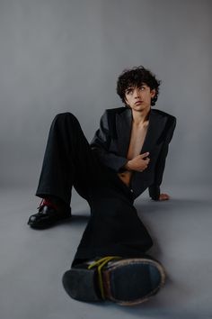 a young man sitting on the ground with his shirt off and shoes in front of him