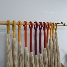 several different colors of tassels hanging on a wooden rod in front of a white wall