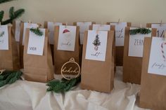 small brown paper bags with christmas cards on them sitting on top of a table next to evergreen branches