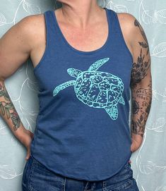 Our hand-drawn Sea Turtle design is printed in teal on this super soft royal blue eco tri-blend racerback tank. Straight through the body. Overlock hem. 40% tencel model (plant fibers), 35% cotton, 25% recycled poly. Sizes available: XS, SM, MED, LRG, XL, 2X.  Runs true to size for form fitting, order up for a looser fit.  Model is a size Medium/ Large and wearing a medium. Our original, hand-drawn designs are printed on sweat-shop free clothing using environmentally conscious water-based inks. Blue Cotton Racerback Tank Top, Casual Blue Printed Tank Top, Fitted Casual Tank Top With Screen Print, Casual Fitted Tank Top With Screen Print, Blue Racerback Top With Graphic Print, Blue Crew Neck Tank Top For Beach, Blue Crew Neck Tank Top For The Beach, Blue Graphic Print Racerback Tank Top, Blue Racerback Tank Top With Graphic Print