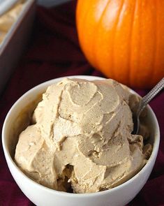 a white bowl filled with peanut butter next to a pumpkin on a red table cloth