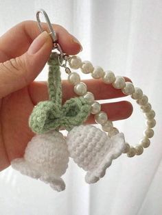 a hand holding a crocheted keychain with two bells attached to it