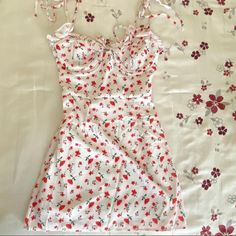 a dress laying on top of a bed next to a white sheet with red flowers