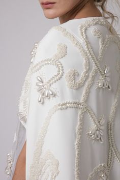 the back of a woman's white dress with beading and pearls on it