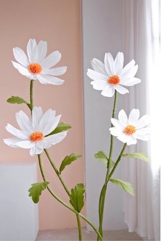 three white daisies in a vase on a window sill next to a pink wall