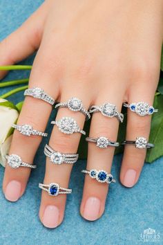 a woman's hand with five different rings on top of her fingers and two roses in the background