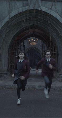 two people running in front of an archway with vines on the wall and one person wearing a tie