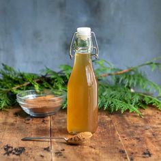 a glass bottle filled with liquid sitting on top of a wooden table next to a bowl