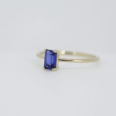 a gold ring with a blue stone in the center on a white surface, it has a thin band