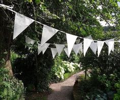 white bunting flags hanging over a path in a garden with trees and flowers around it