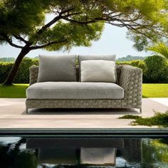 a couch sitting on top of a patio next to a tree and swimming pool in front of it