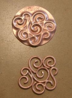 two metal circles sitting on top of a table next to each other, one with an intricate design in the middle