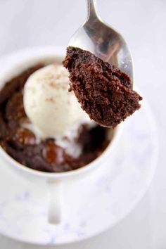 a spoon with some ice cream on top of a chocolate cake in a cup and saucer