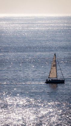 a small sailboat floating in the middle of the ocean with sun reflecting off the water