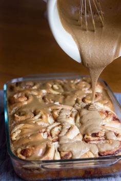 a person pouring caramel sauce on top of a cinnamon roll in a baking dish