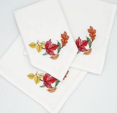 three white napkins with embroidered leaves on them