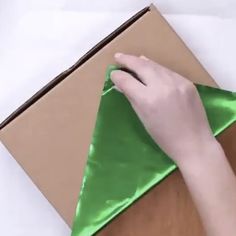 a person is folding an origami piece into a triangle with a green satin ribbon