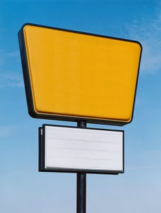 a yellow and white sign sitting on top of a metal pole next to a blue sky