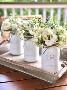 four white mason jars with flowers in them on a wooden tray, ready to be used as centerpieces