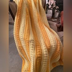 a yellow and white crocheted blanket sitting on top of a couch next to a vase with flowers