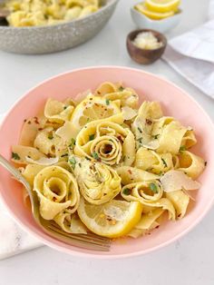 a pink bowl filled with pasta and lemon slices