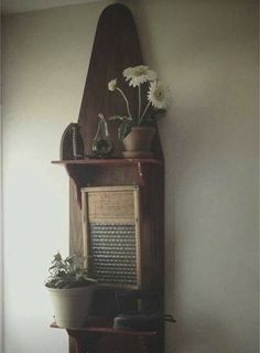 an old wooden shelf with flowers and books on it in front of a white wall