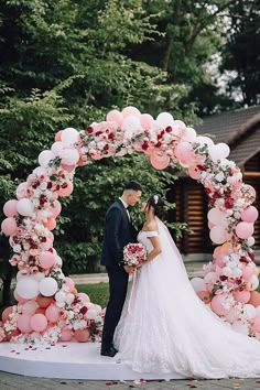 a bride and groom standing in front of a wedding arch decorated with pink and white balloons