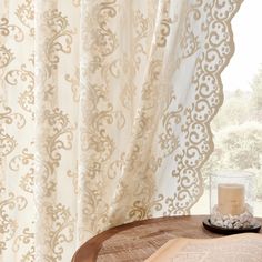 an open book sitting on top of a wooden table next to a window with curtains