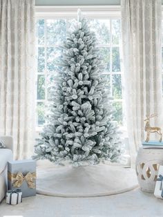 a white christmas tree in front of a window with presents on the floor next to it