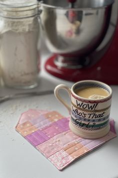 a cup of coffee sitting on top of a coaster next to a mixer and bowl