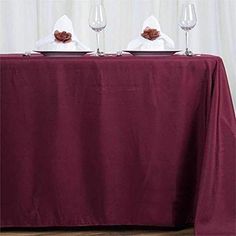 two wine glasses sitting on top of a table covered with a red cloth and white napkins