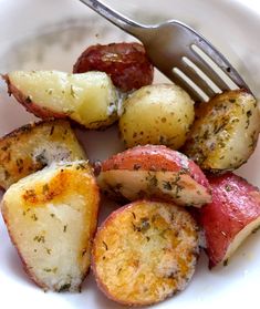 a white plate topped with cooked potatoes and sausages next to a fork on top of a table