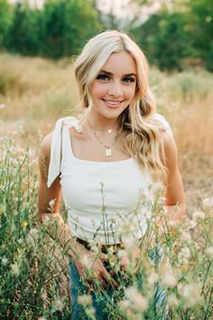 a beautiful blonde woman sitting in the middle of a field with wildflowers and grass