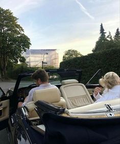 two people are sitting in the back of a convertible car and one person is driving