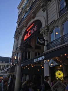 people are standing outside the front of an alcove restaurant at dusk with lights on