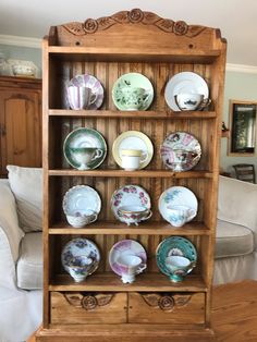 a wooden shelf filled with plates on top of a hard wood floor next to a white couch