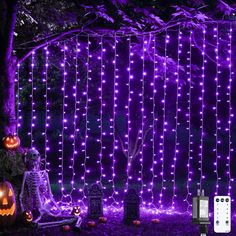 halloween decorations with purple lights and pumpkins on the ground in front of a tree